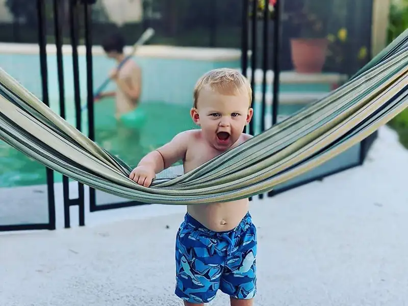 toddler hanging on hammock outside of pool safety fence