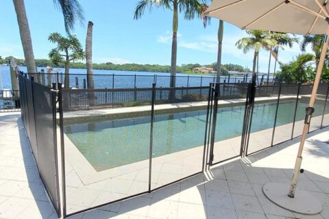 A pool fence surrounds a patio area with an umbrella and chairs for relaxation.