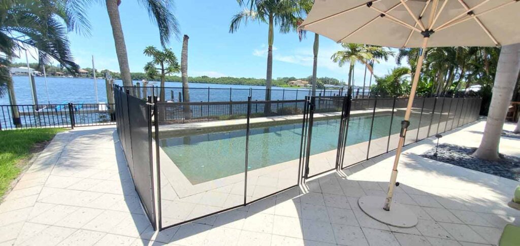 A pool fence surrounds a patio area with an umbrella and chairs for relaxation.