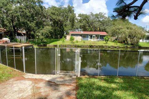 A serene pond surrounded by a wooden fence, with a house visible in the background.