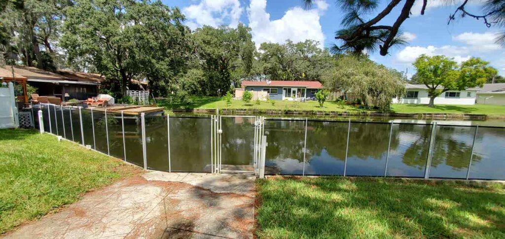A serene pond surrounded by a wooden fence, with a house visible in the background.