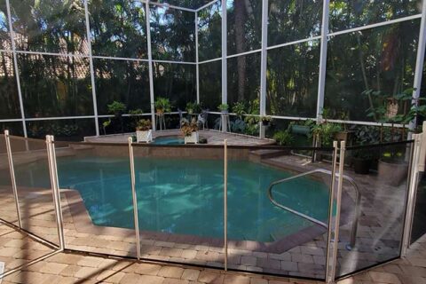 A swimming pool surrounded by a fence, with a patio area visible nearby.