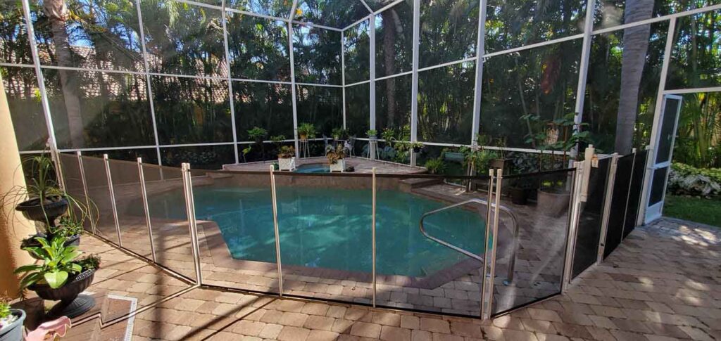 A swimming pool surrounded by a fence, with a patio area visible nearby.